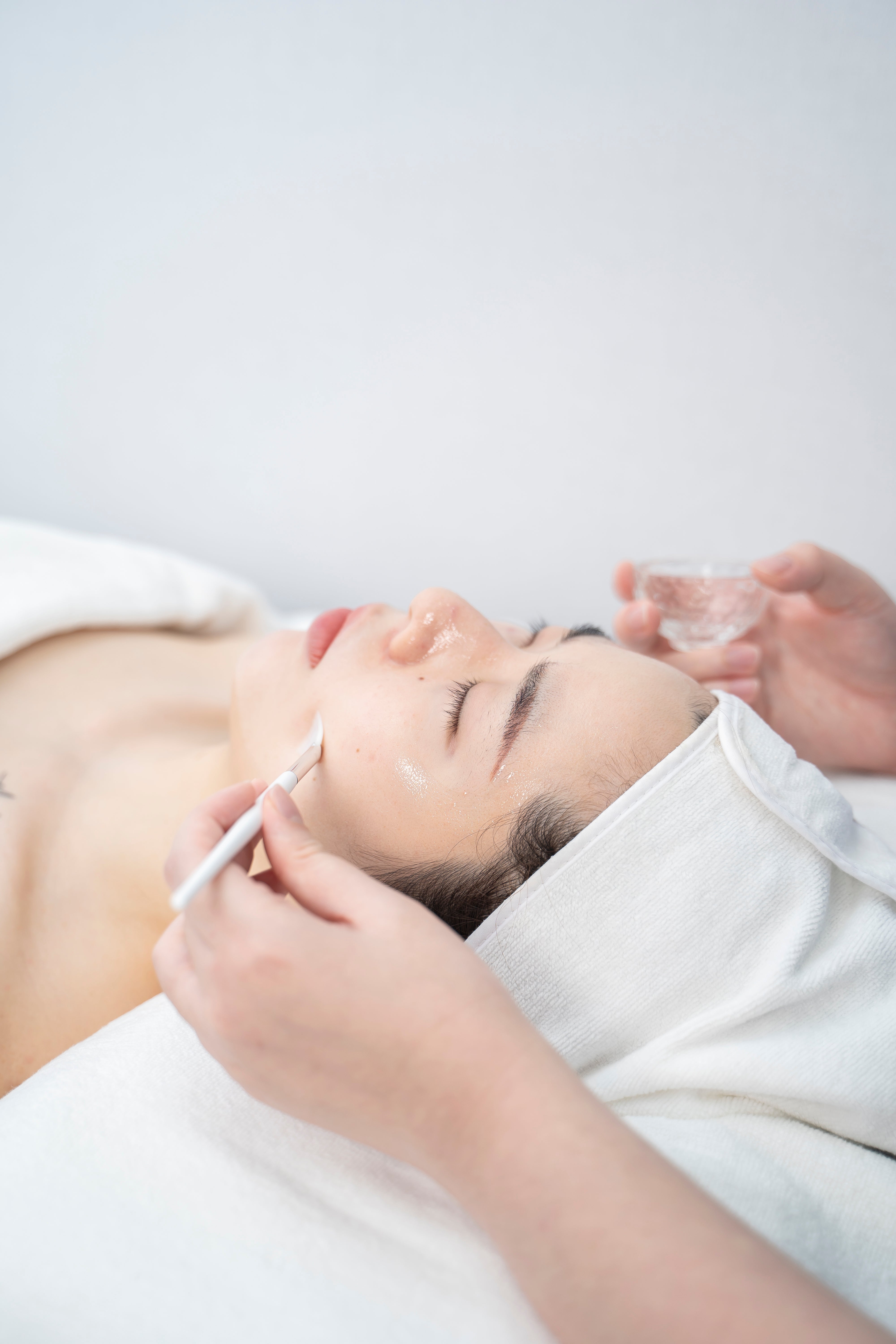 Person receiving a facial treatment with a white towel on a light gray background