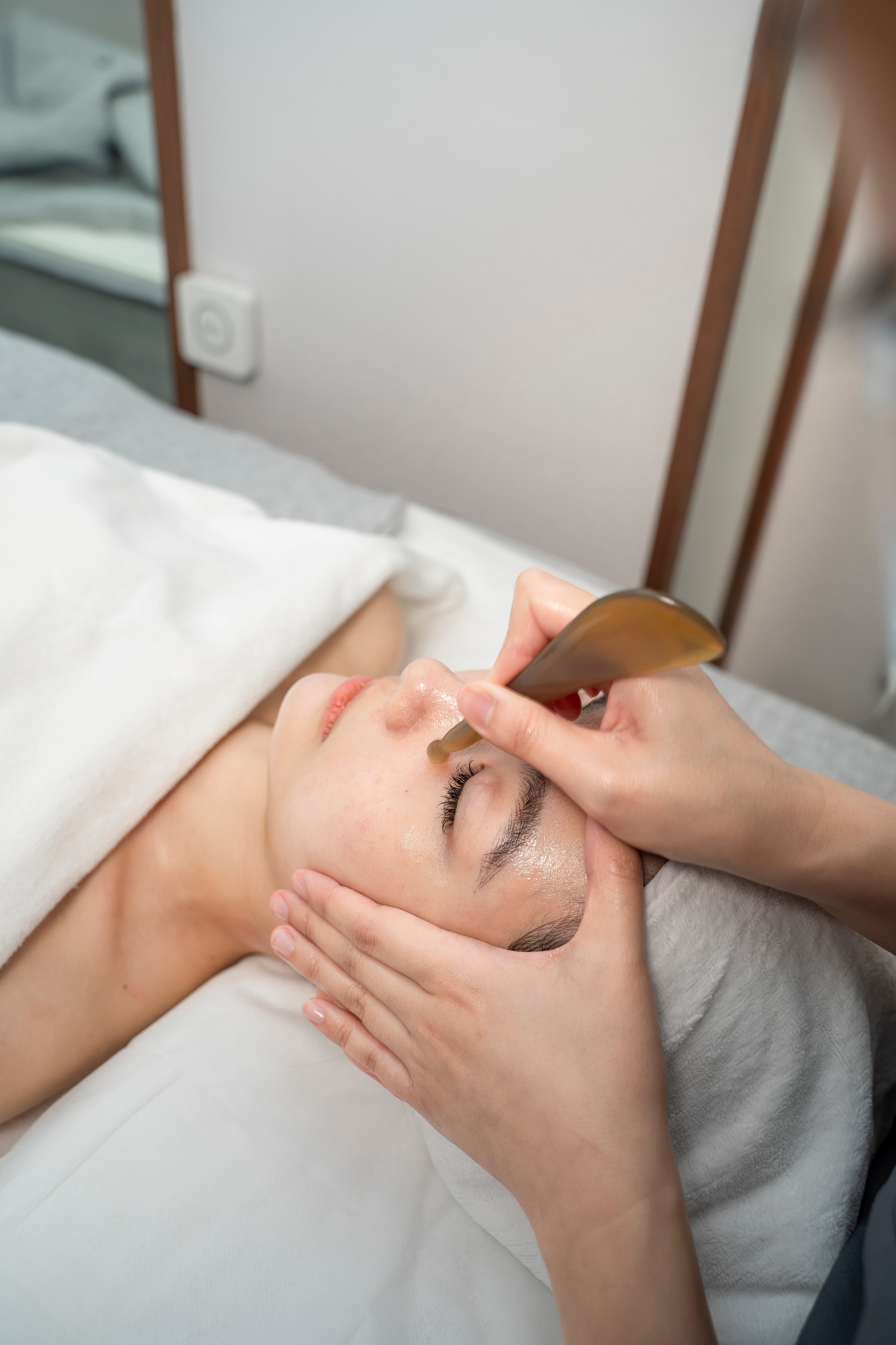 Person receiving a facial treatment with a wooden tool in a spa setting