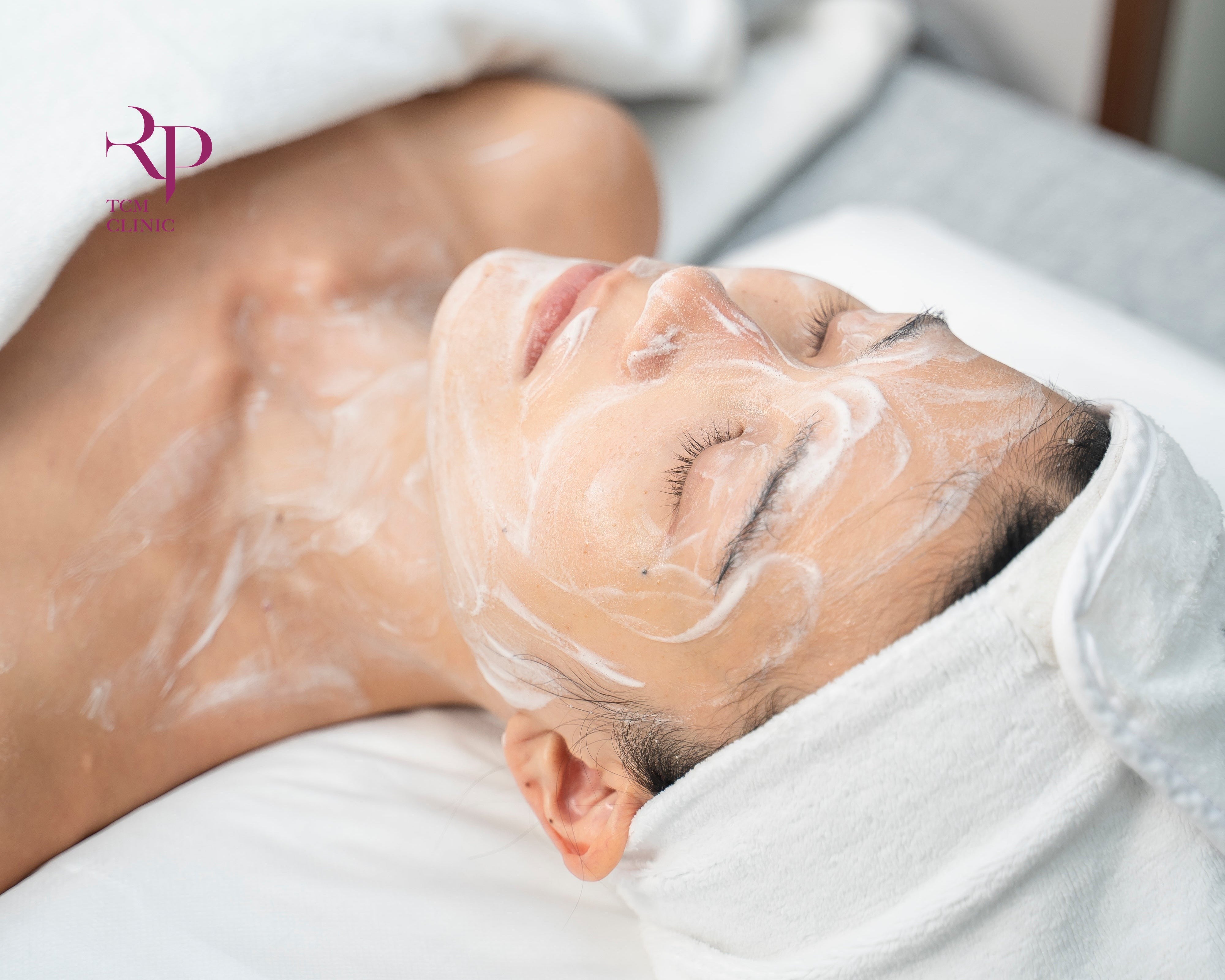 Person receiving a facial treatment with a white towel draped over them.