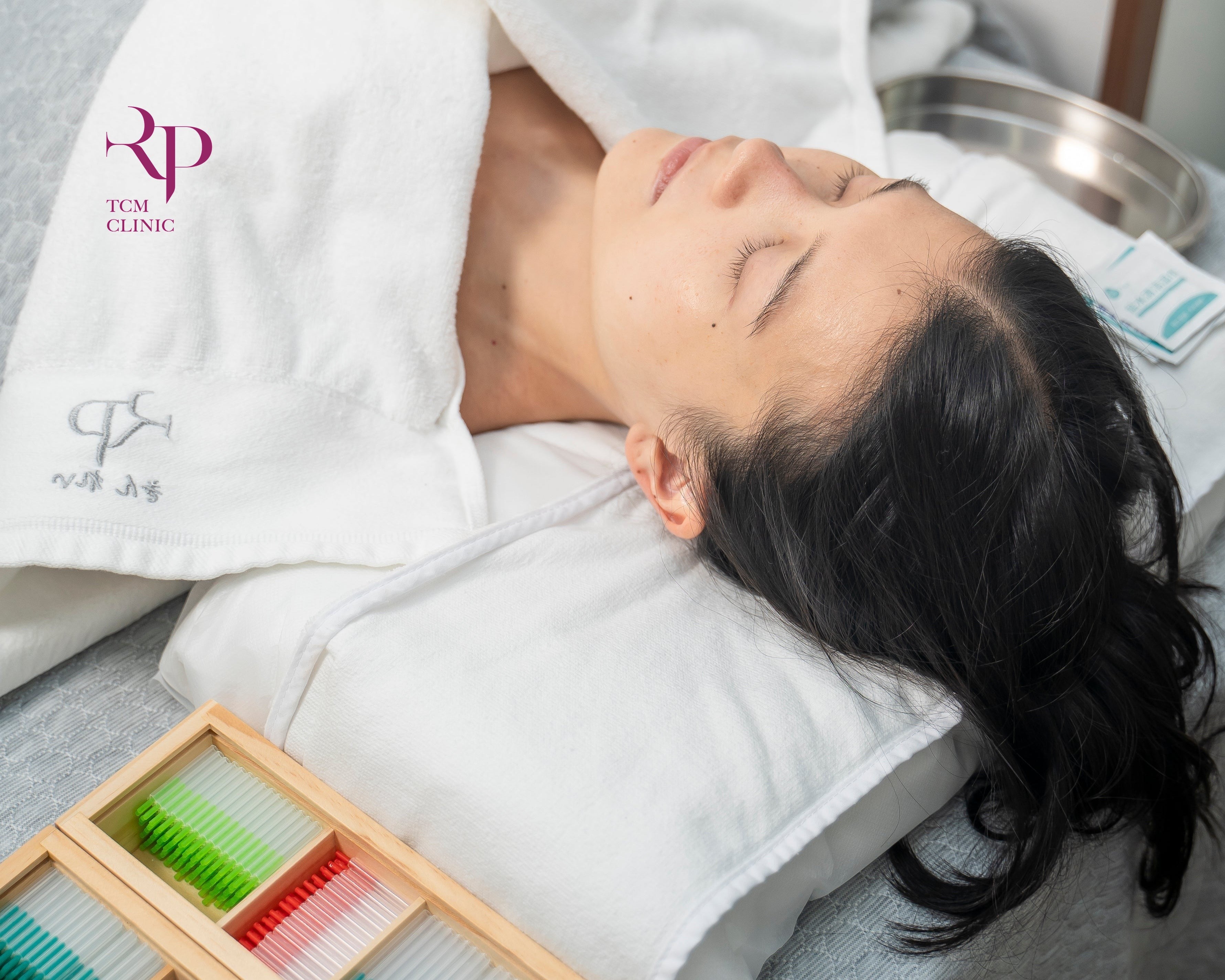 Person receiving a facial treatment with a box of colorful threads on a table.