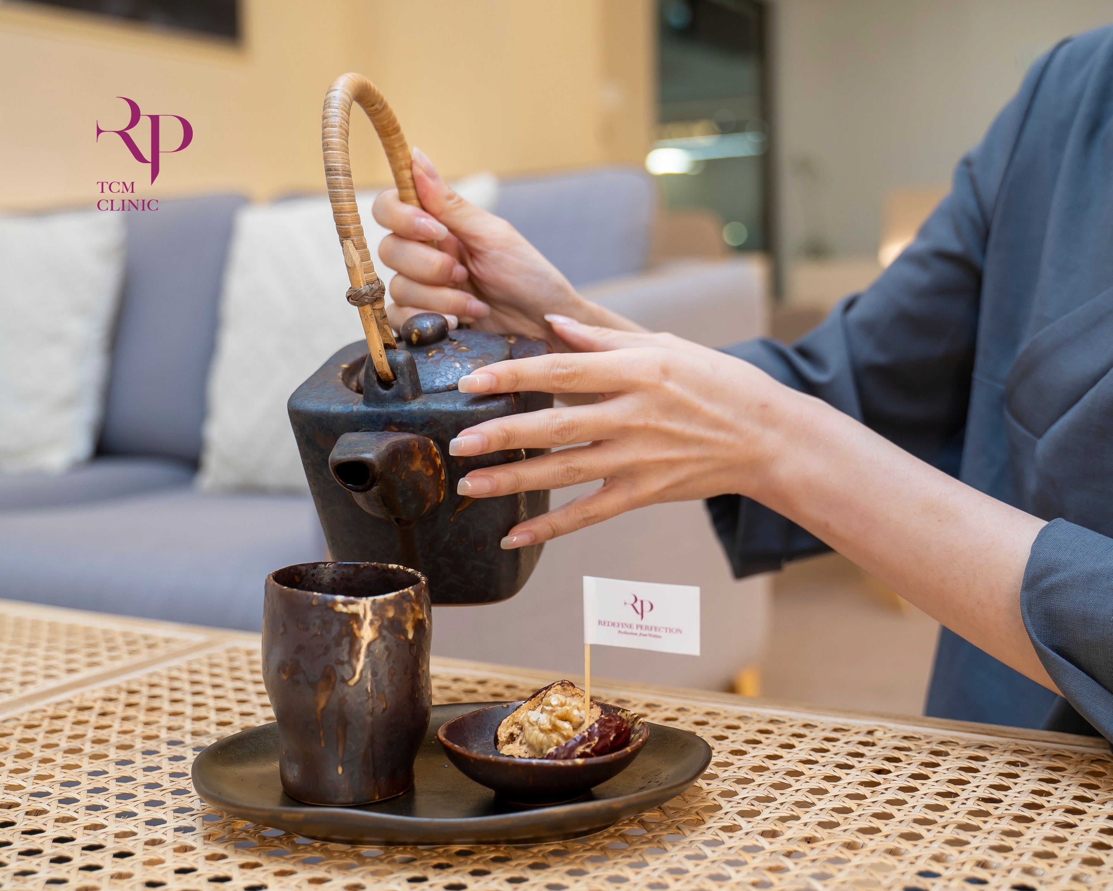 Person holding a traditional teapot on a woven table with a blurred indoor setting