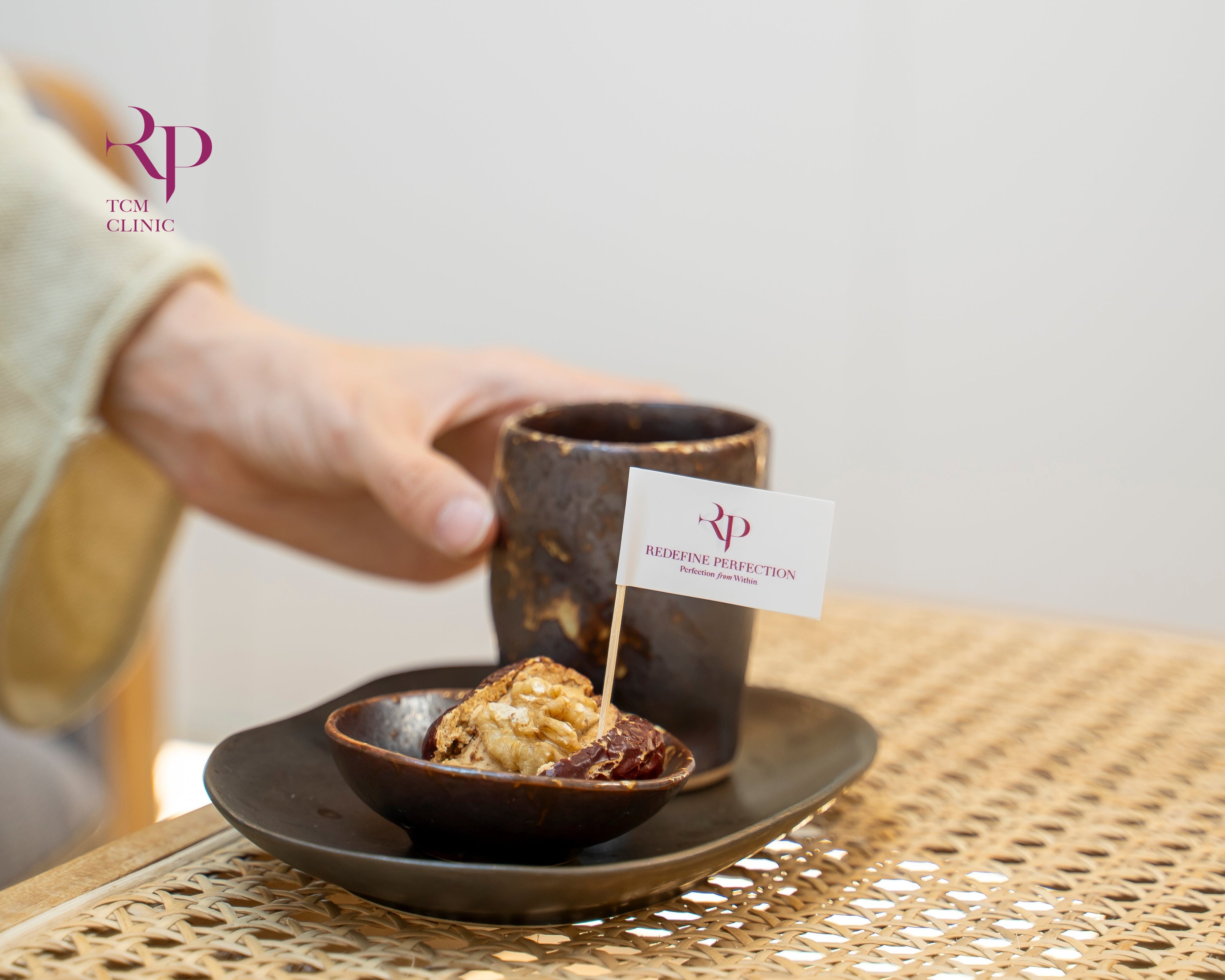 Person holding a cup with a small dish of food on a woven surface