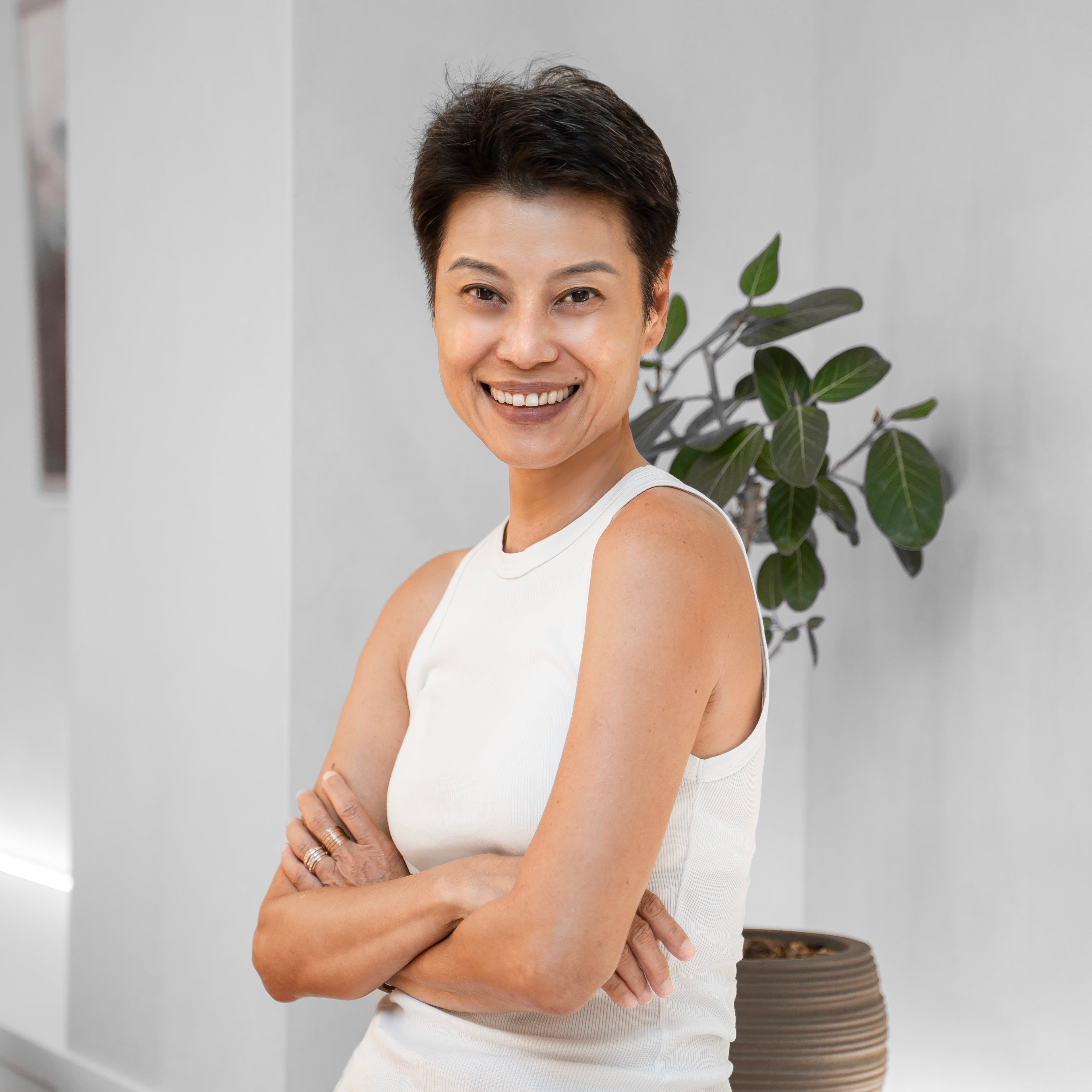 Woman in a white top and pink skirt standing in a room with a plant and table.