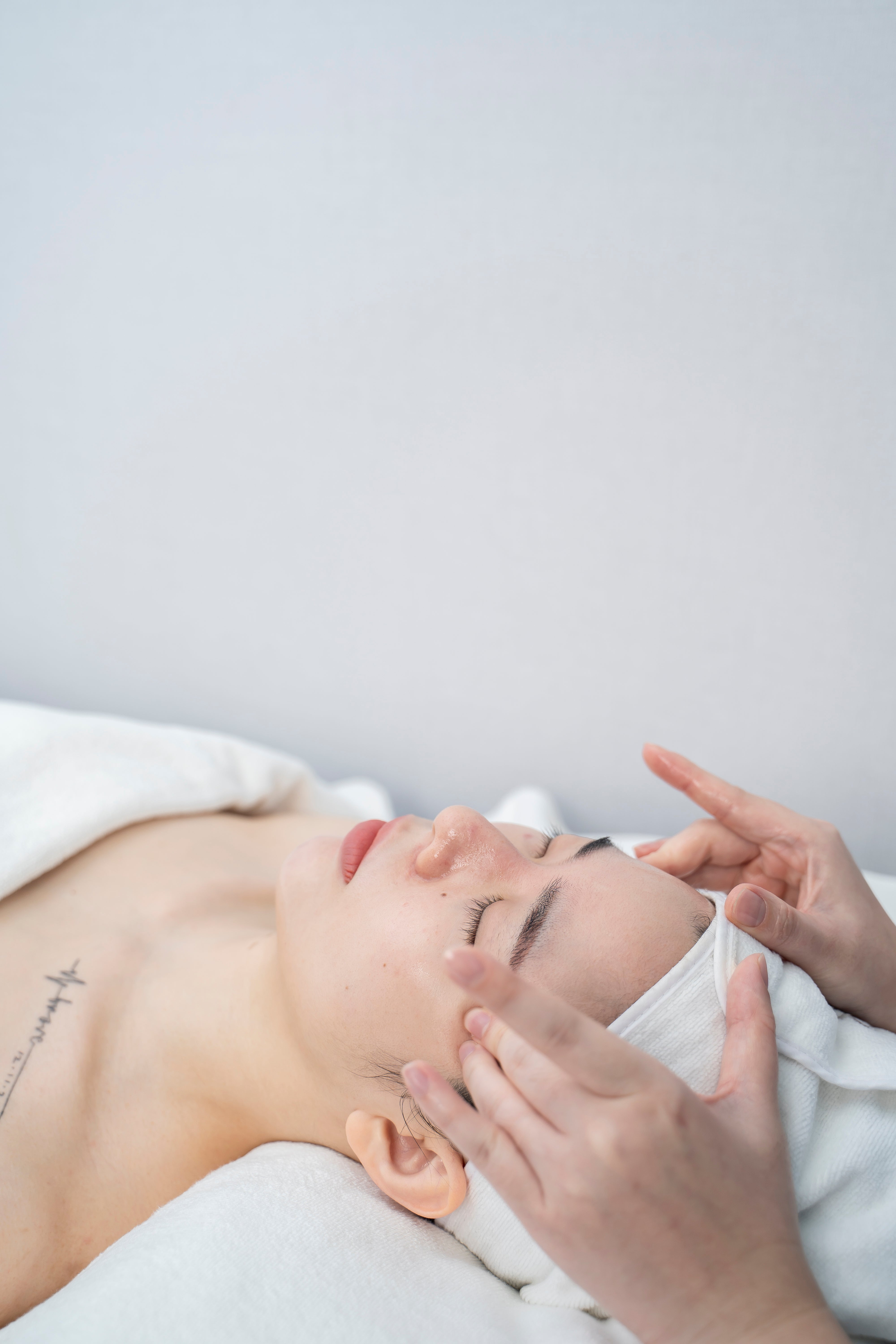 Person receiving a facial treatment with a white towel on a neutral background