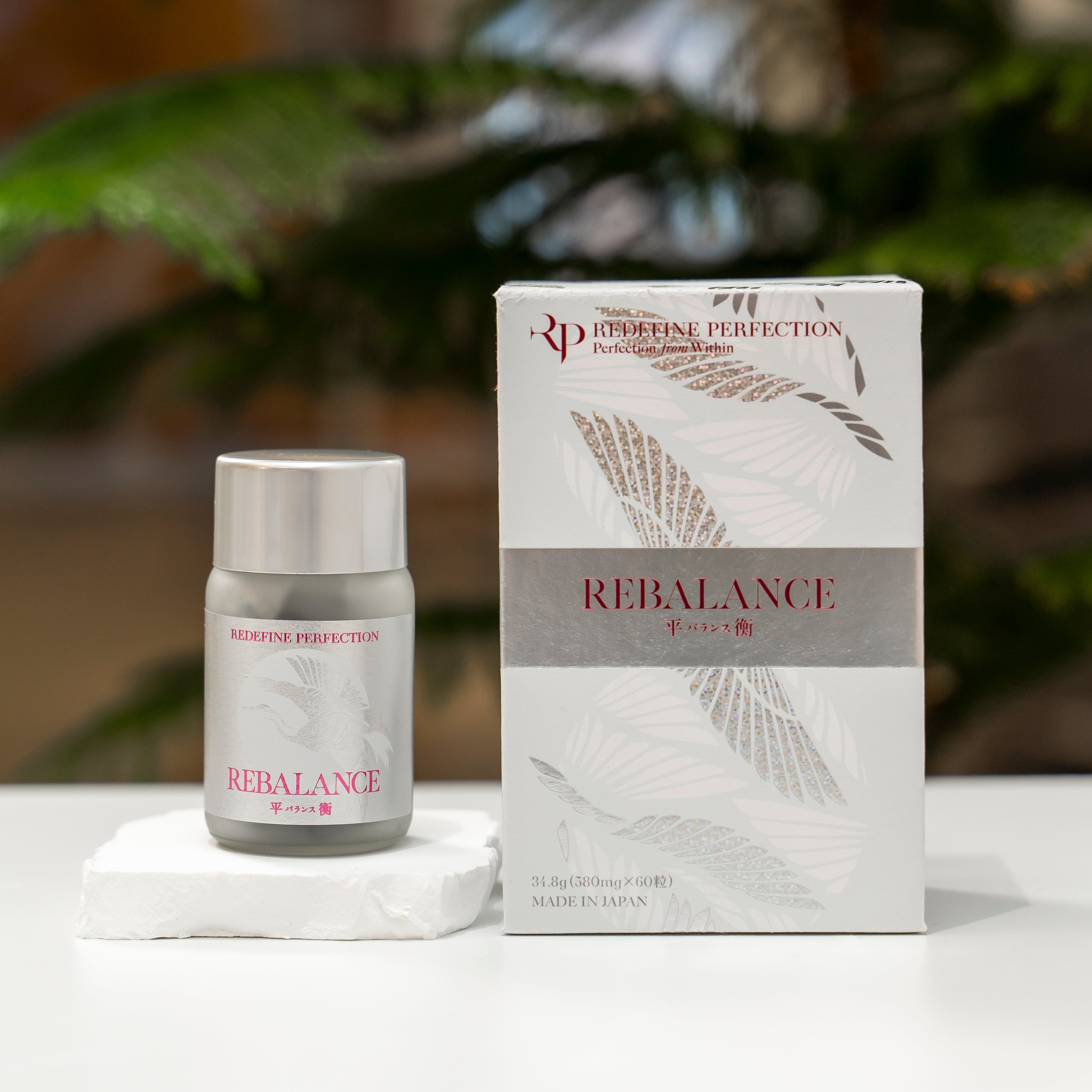 Skincare product and packaging labeled 'Rebalance' on a white surface with a blurred plant background.