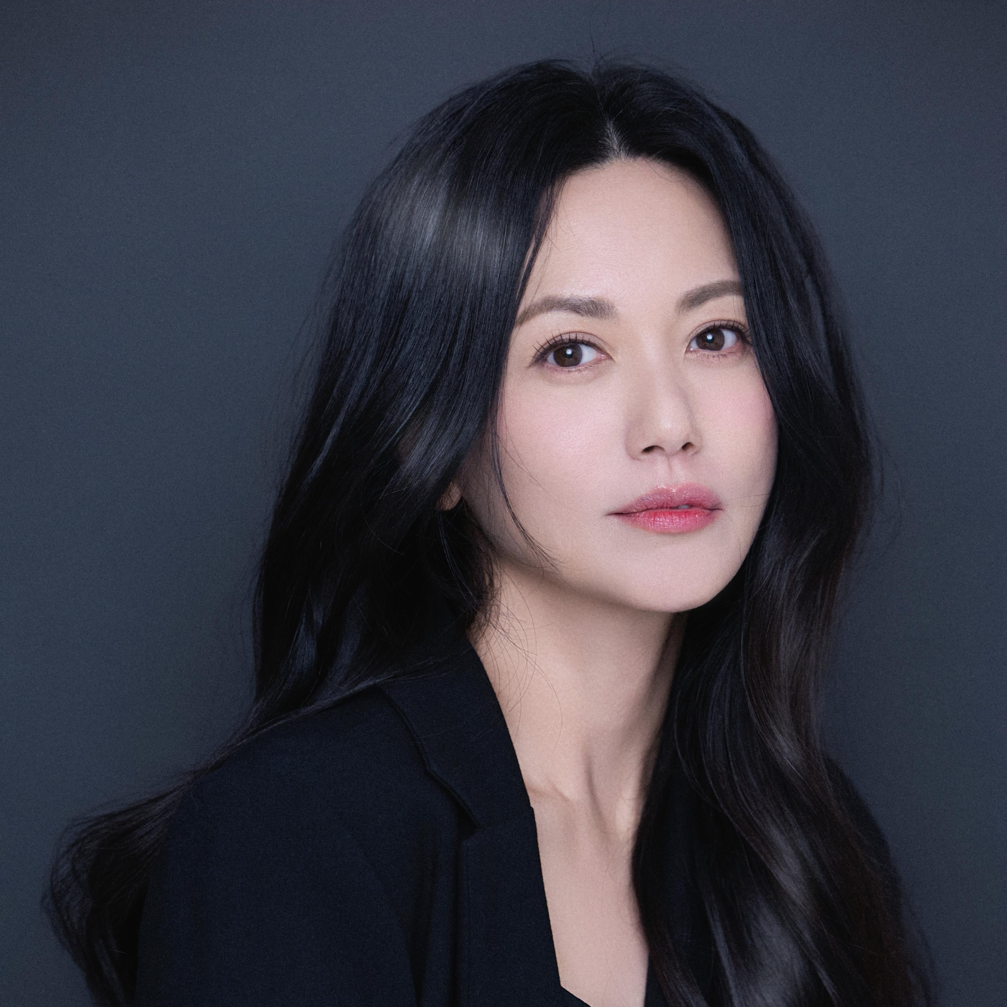 Woman with long black hair wearing a black outfit against a dark background