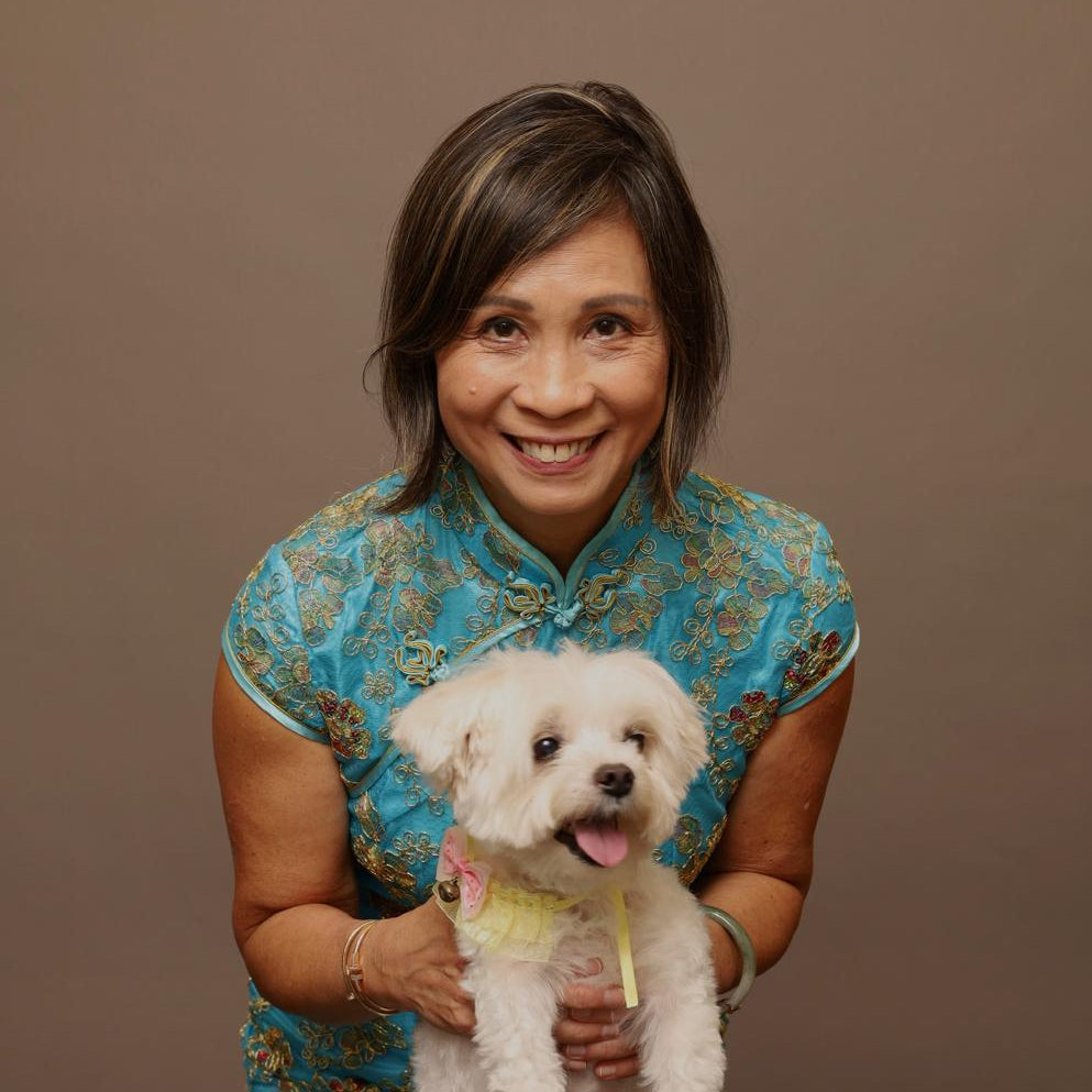 Woman in a blue floral dress holding a small white dog against a brown background