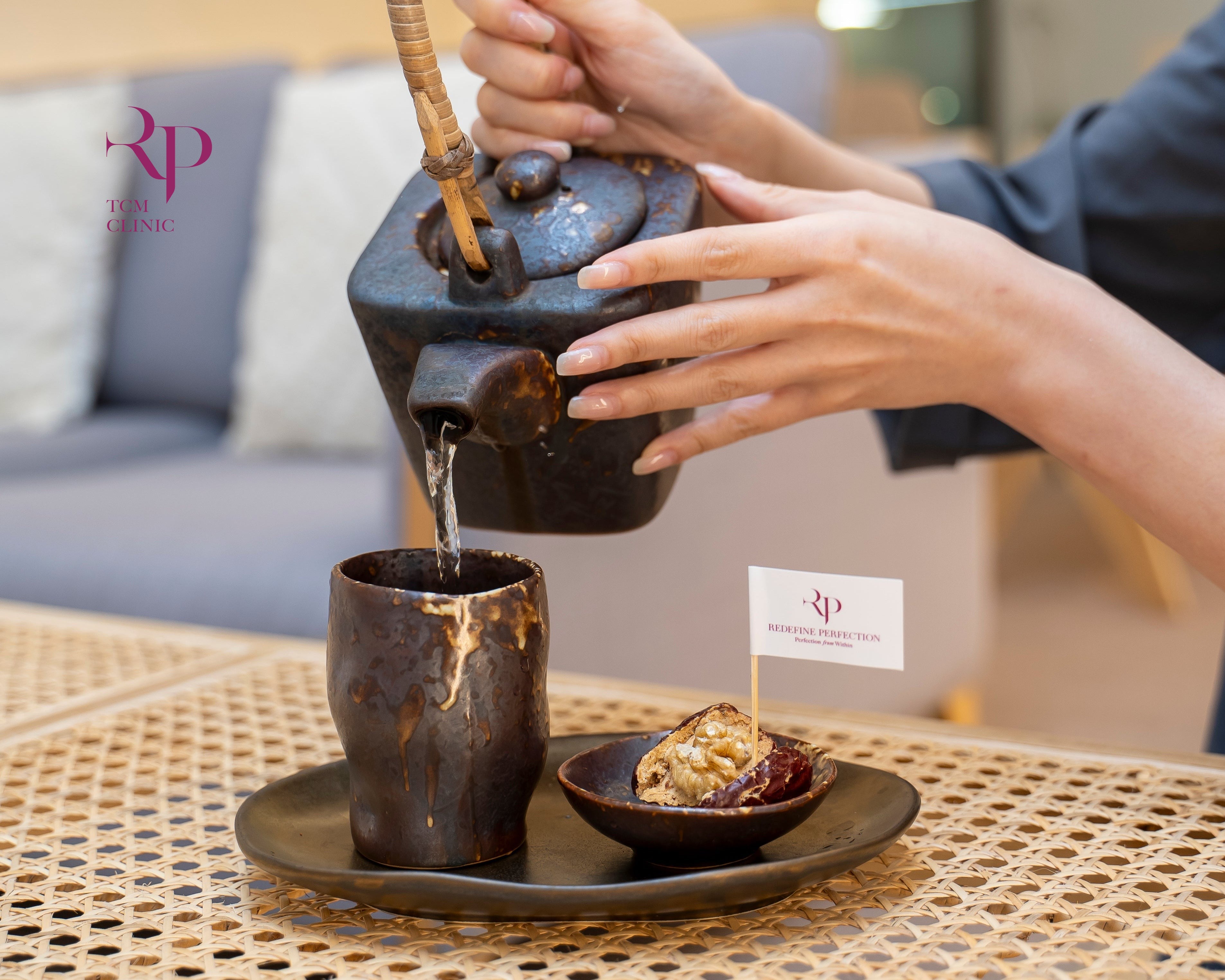 Person pouring tea from a traditional teapot into a cup on a woven table.